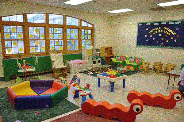 Kindergarten Room Interior With Drawings And Colorful Chairs, Tables On The Floor.